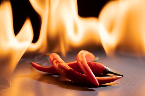 Red chili peppers. Sharp red siliculose pepper against a flame. With reflection in a mirror.